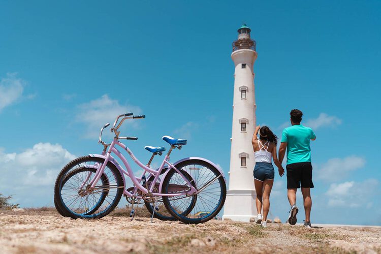 Two bikes and a couple standing in front of a lighthouse